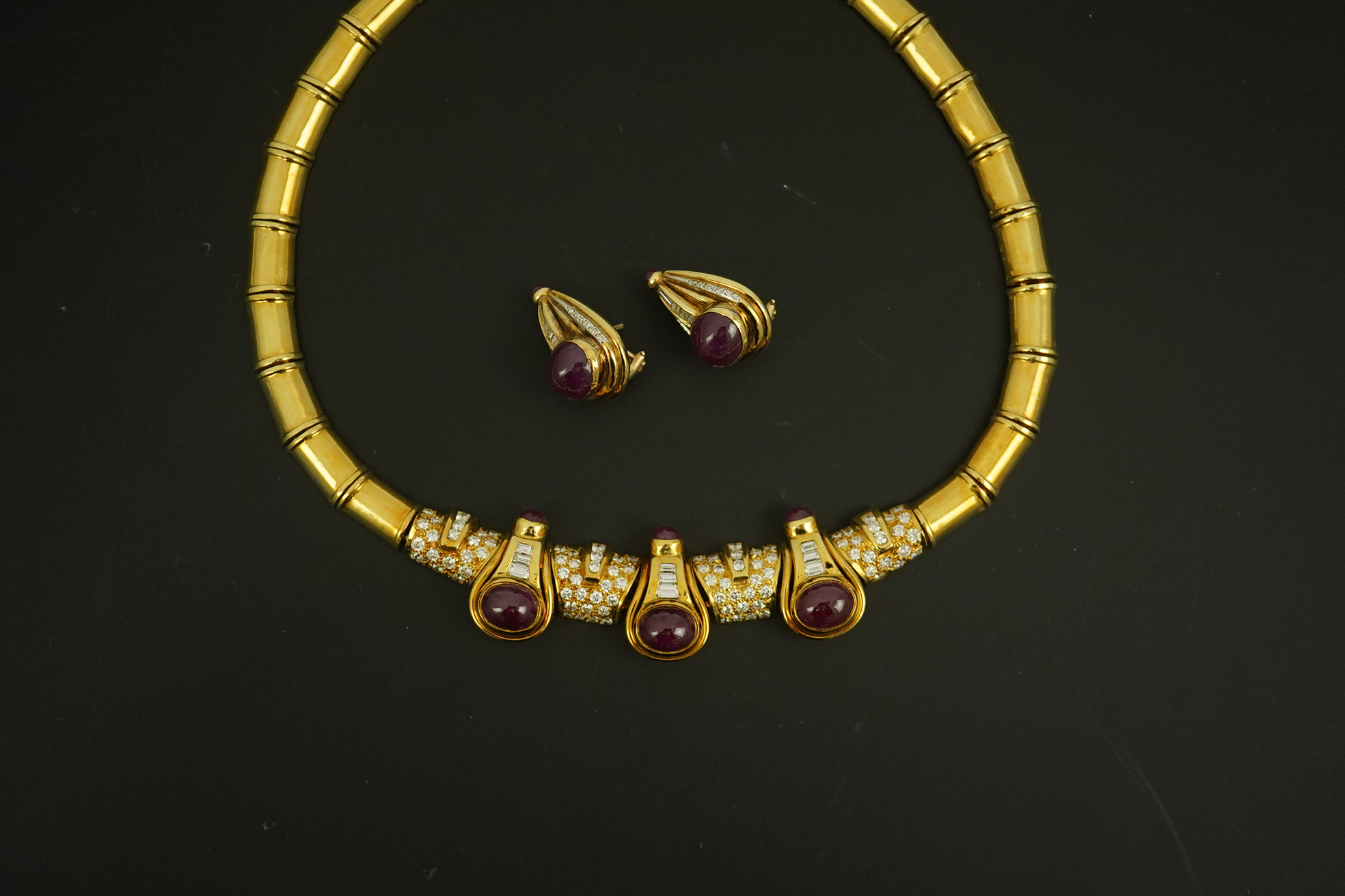 A modern 18k gold, cabochon ruby, round and baguette cut diamond cluster set torque necklace and a pair of matching earrings